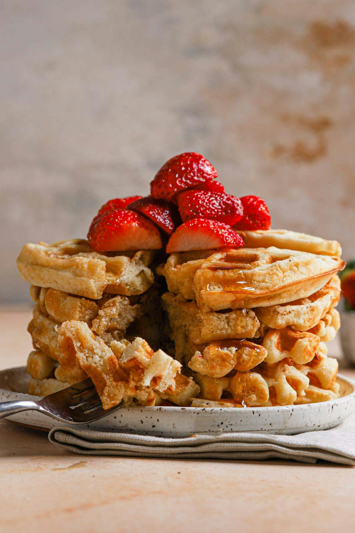stack of belgian waffles topped with strawberries on a plate