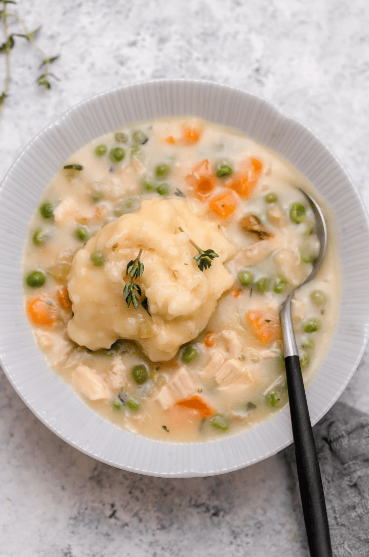 overhead image of a serving of chicken and dumplings in a white bowl with a spoon