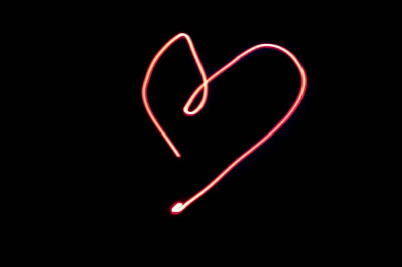 A red heart shape drawn with light against a solid black background