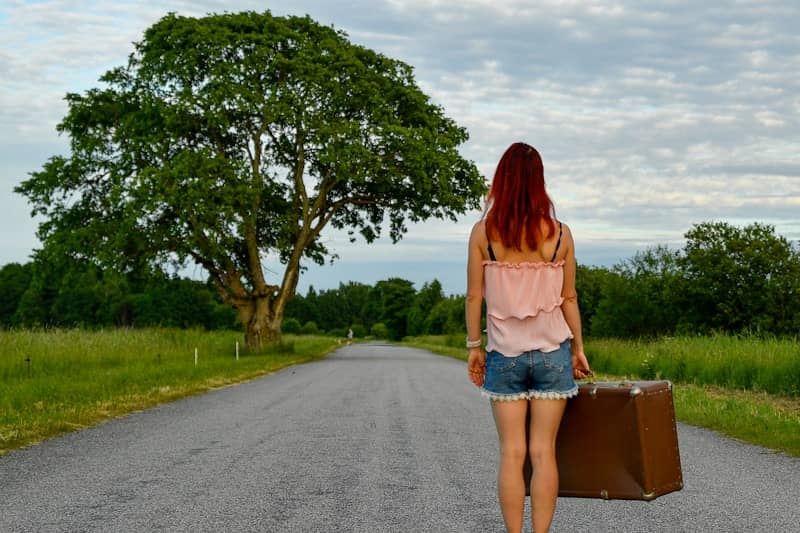 Woman carrying a suitcase walks away on a country road.