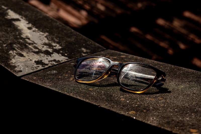 A pair of eyeglasses with dark frames resting on a weathered stone ledge