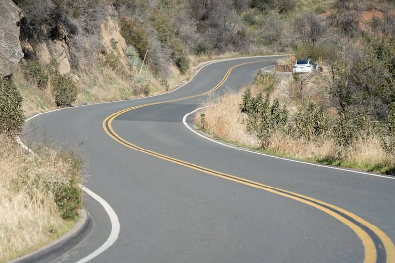 A winding road curves through dry hills under sunlight.