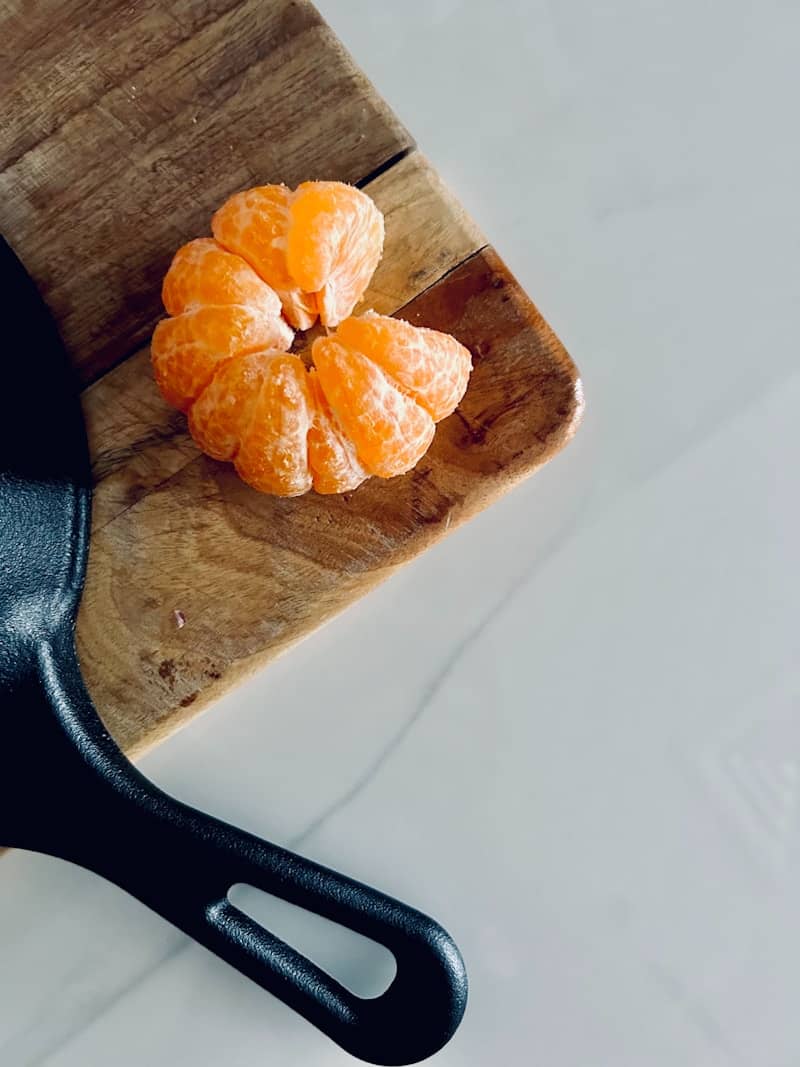 Peeled tangerine on a wooden cutting board next to pan.