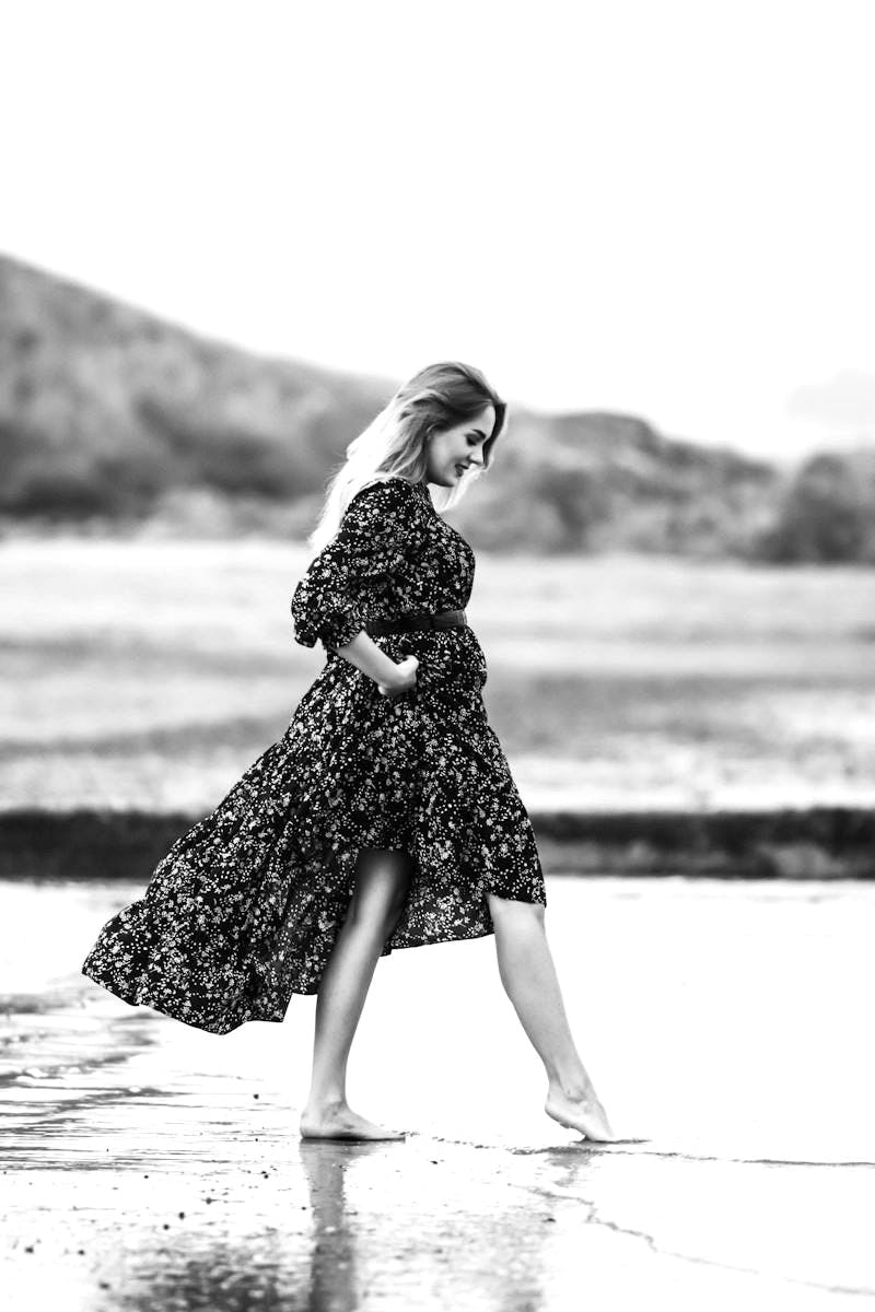 woman in black and white floral dress standing on seashore during daytime