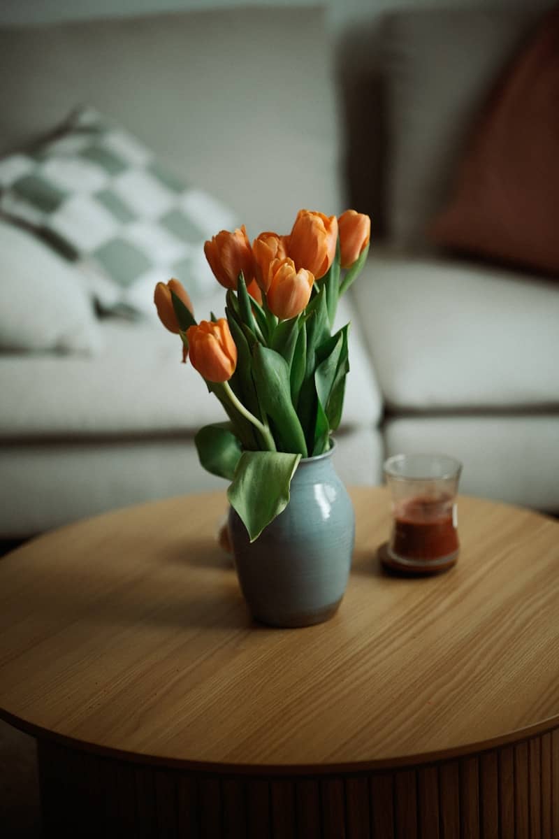 Orange tulips in a vase on a coffee table.