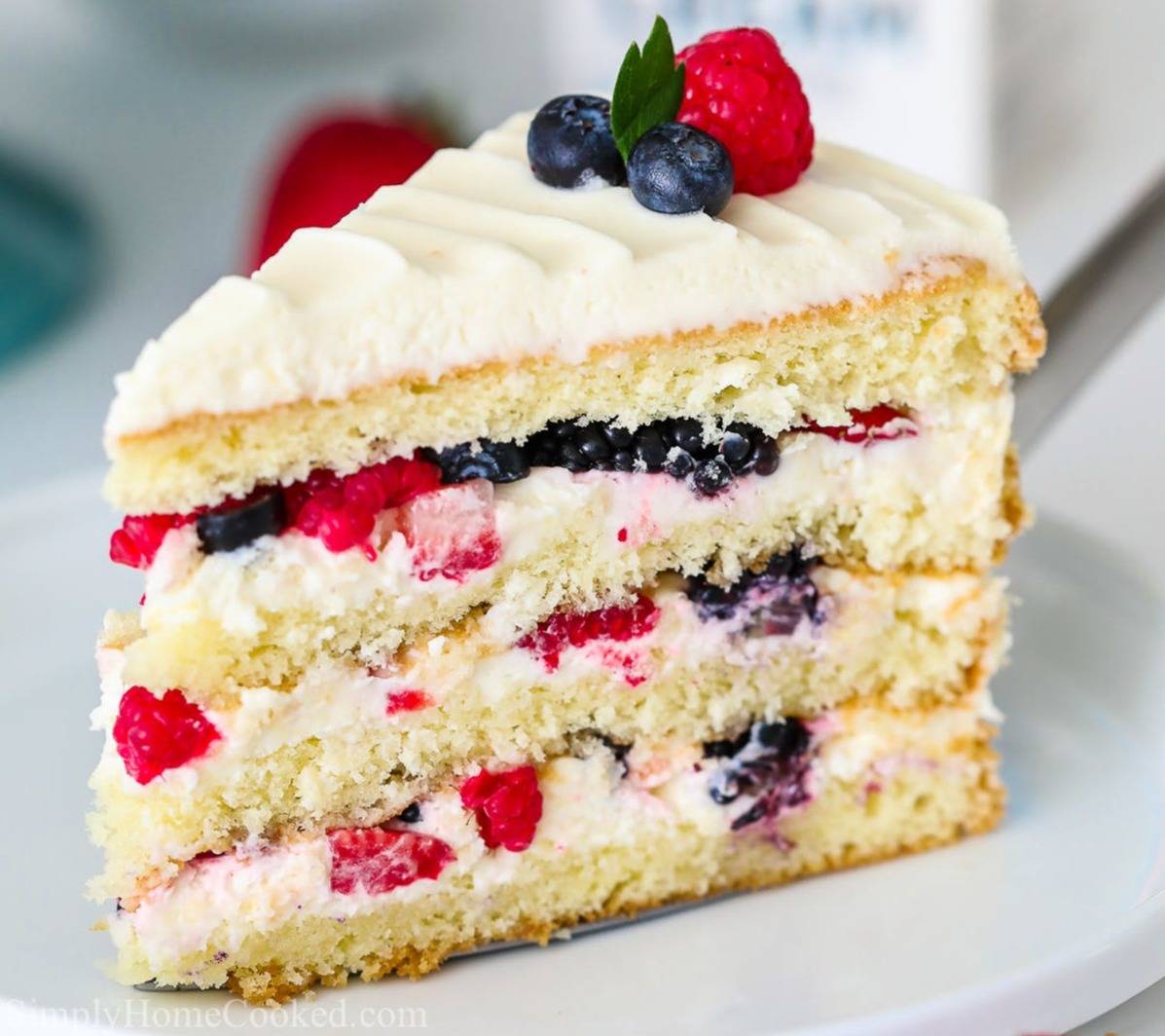 a slice of berry cake with white frosting on a white plate