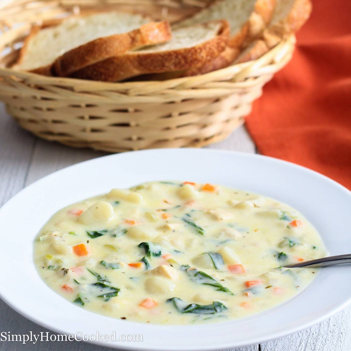 chicken gnocchi soup in a white bowl with a bread basket behind it