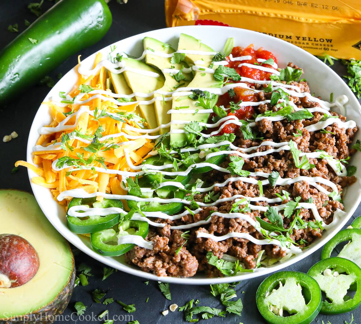 a white plate filled with taco fixings: ground beef, shredded cheddar cheese, lettuce, and a drizzle of sour cream