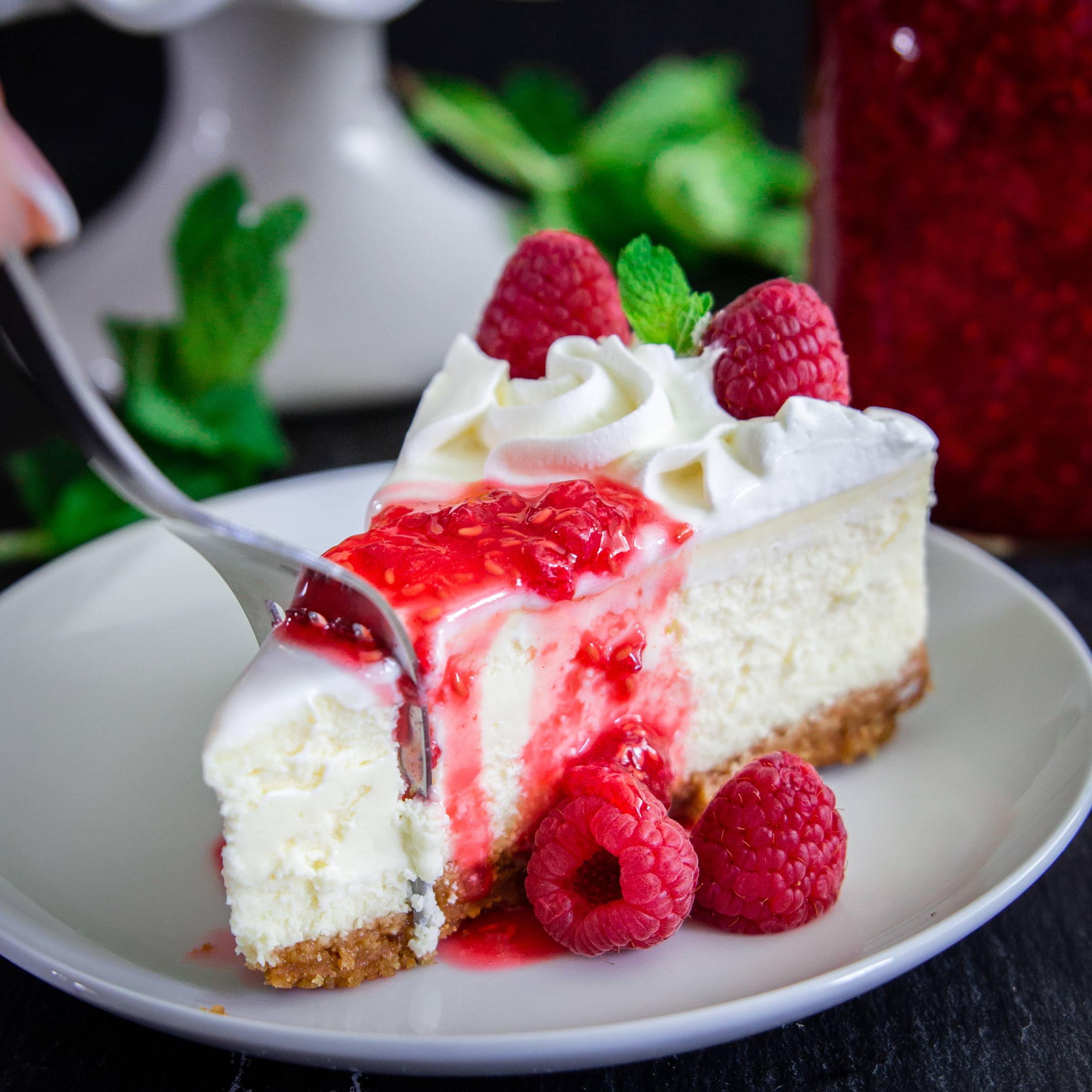 close up image of slice of new york style cheesecake on a white plate with berries around