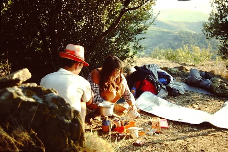 Two people camping, cooking a meal on a portable stove.
