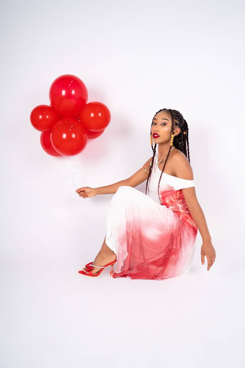 A woman sitting on the ground with a bunch of red balloons