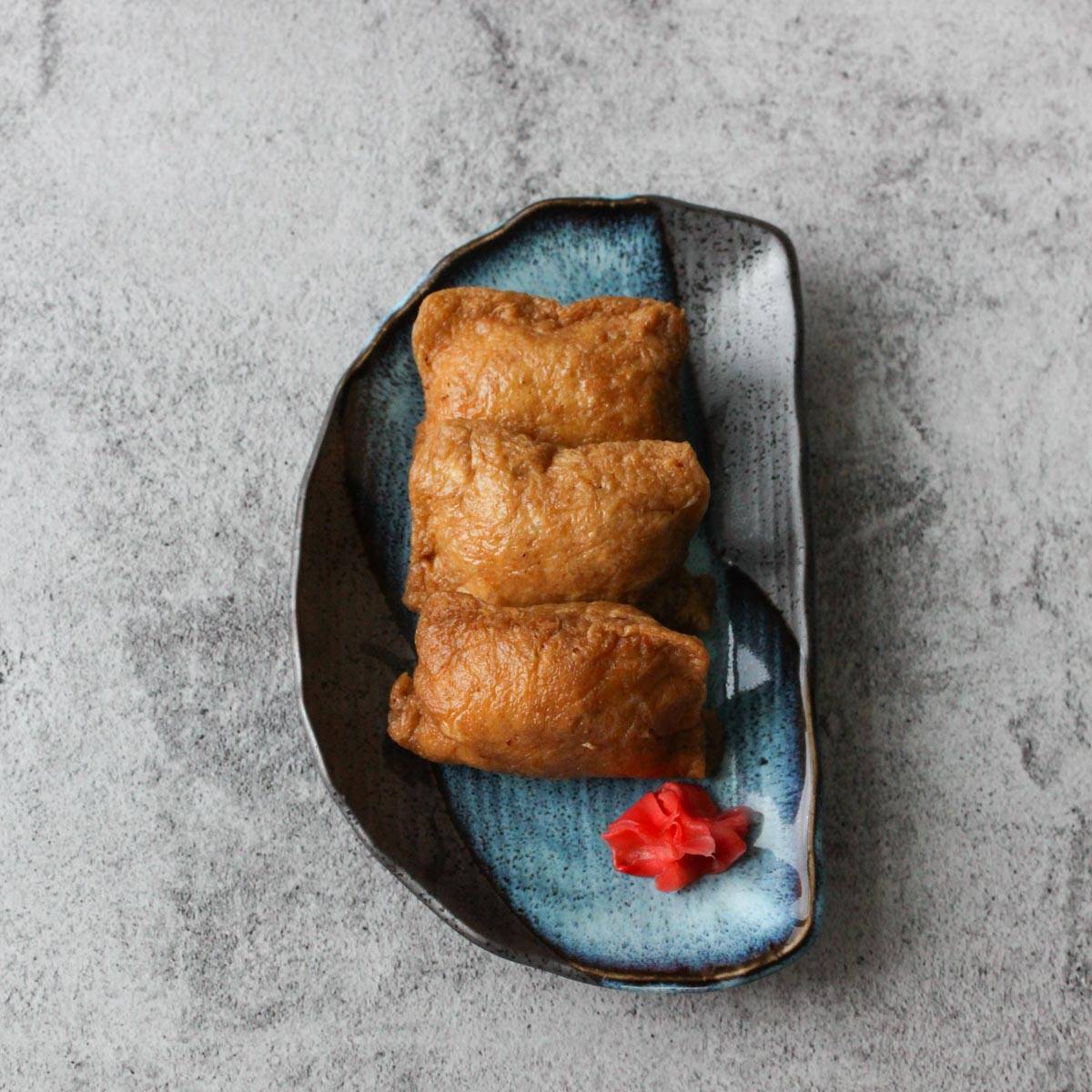 Three inari sushi on a blue plate.