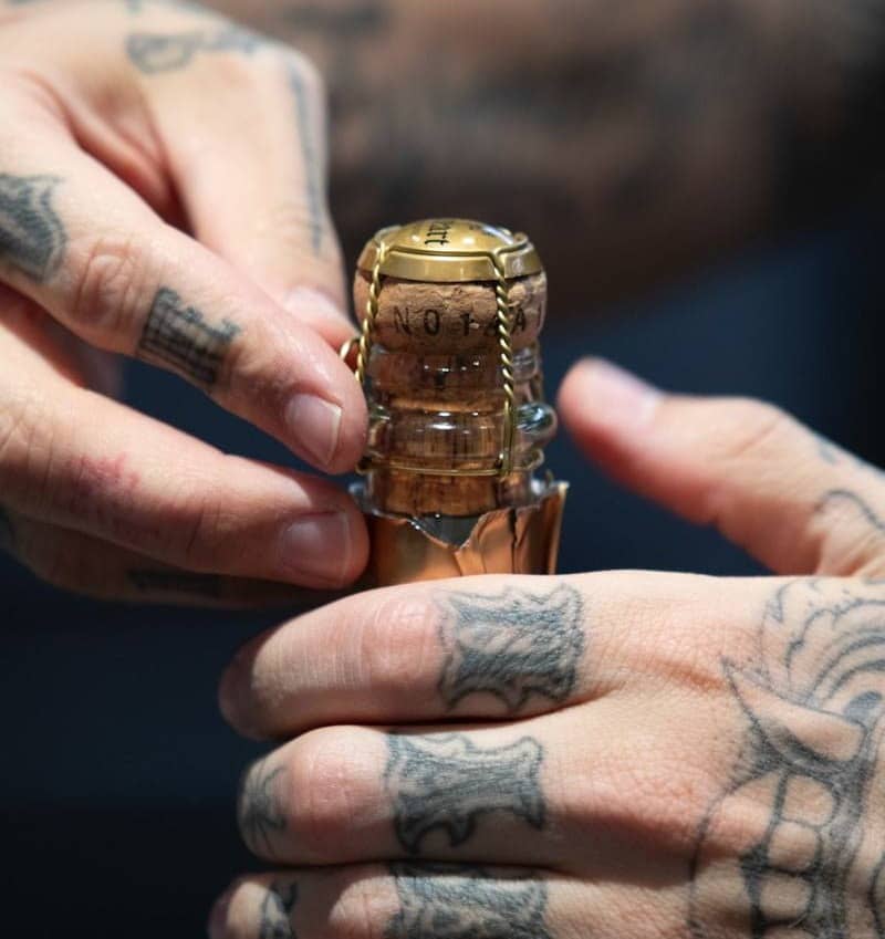 Tattooed hands opening a bottle of champagne.