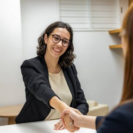 a woman shaking hands with another woman sitting at a table