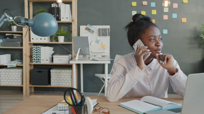 Woman talking on phone at desk in office.
