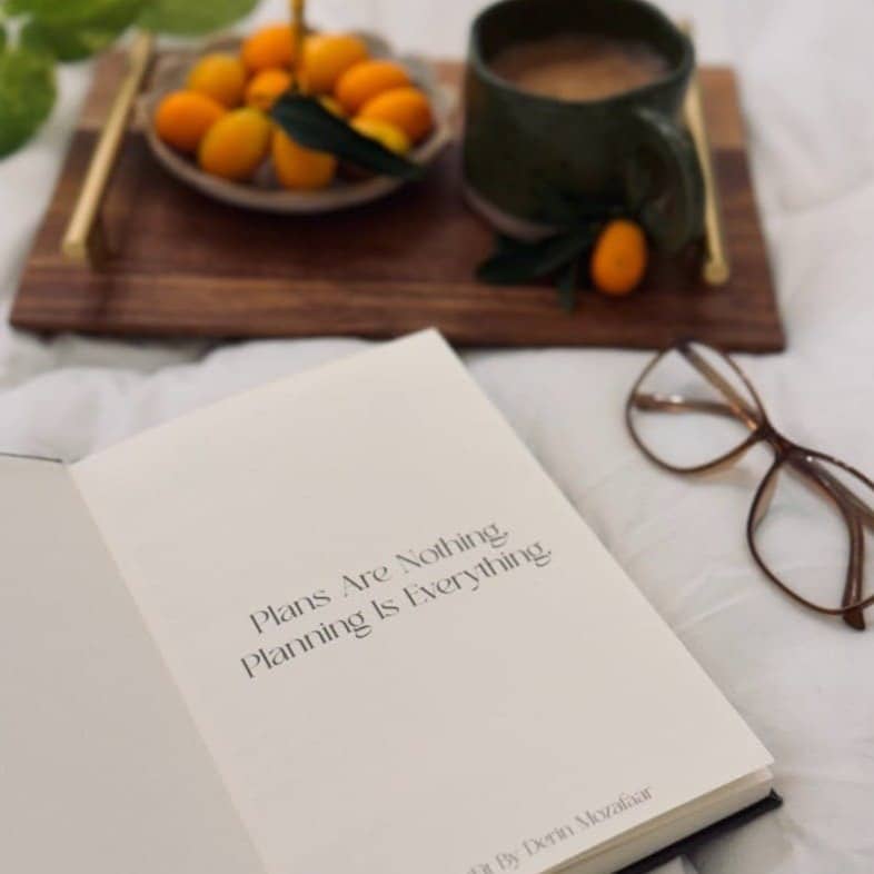An open book sitting on top of a bed next to a bowl of fruit