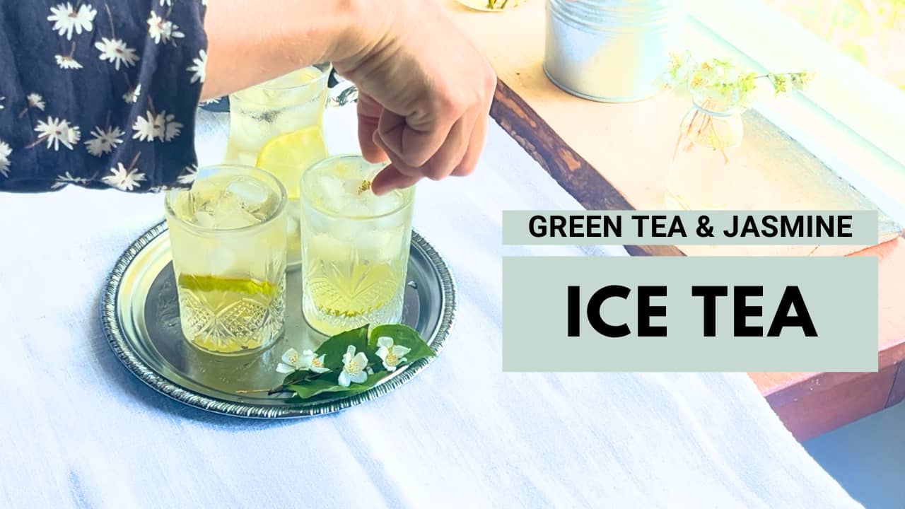 A woman iss setting a jasmine bud on an iced jasmine green tea glass, on a tray.