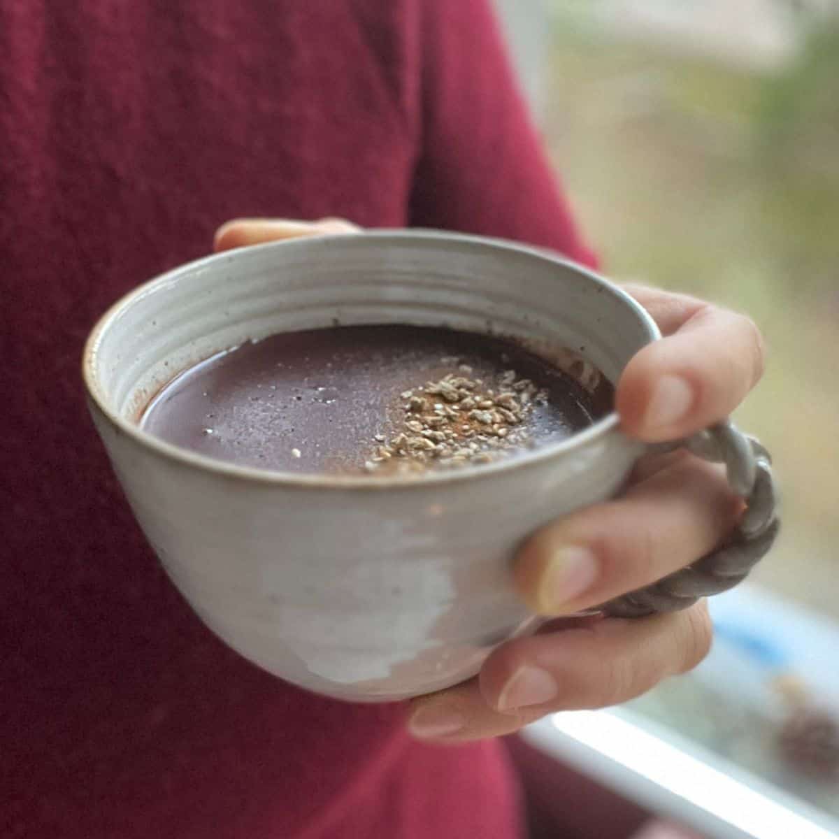 A womna holding a mug with homemade tahini hot chocolate.