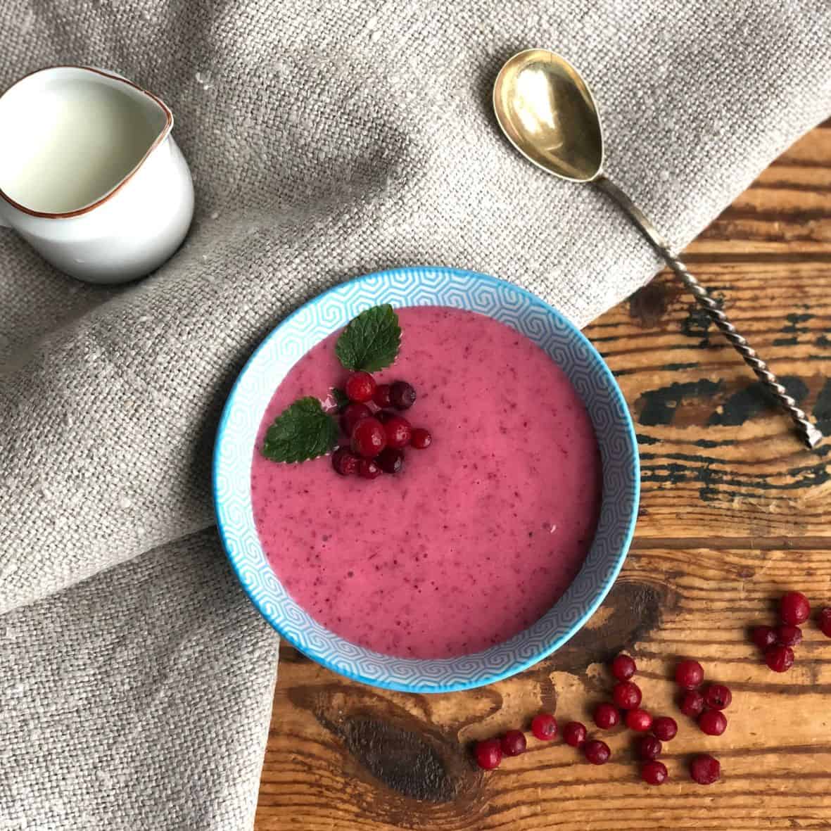 Whipped Lingonberry semolina porridge in a bowl with milk on the side.
