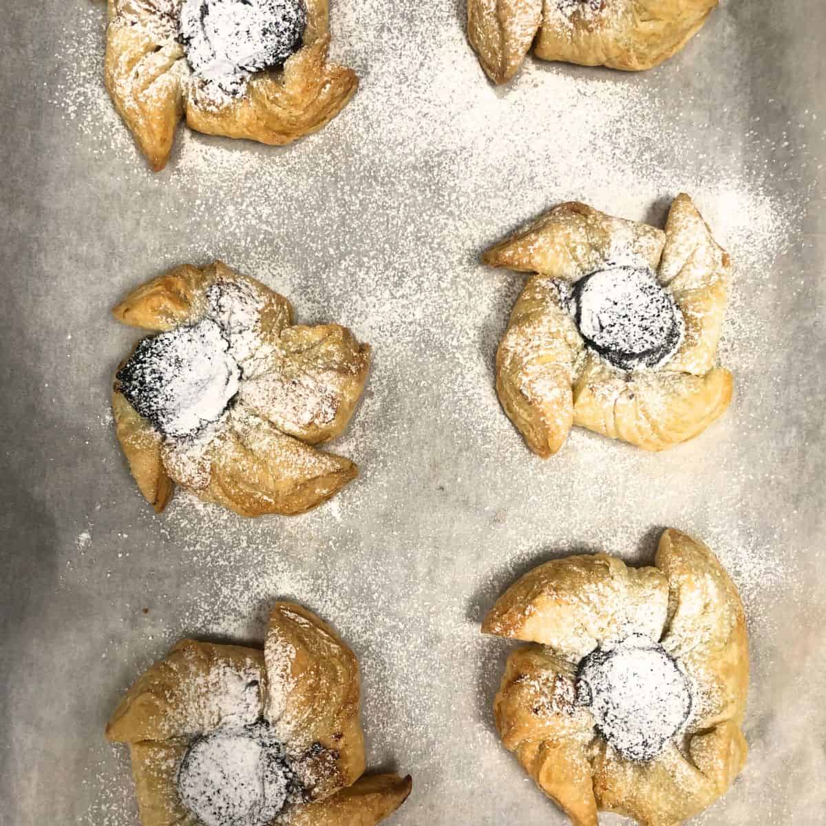 Plum pinwheel tarts dusted with icing sugar on a parchment paper.