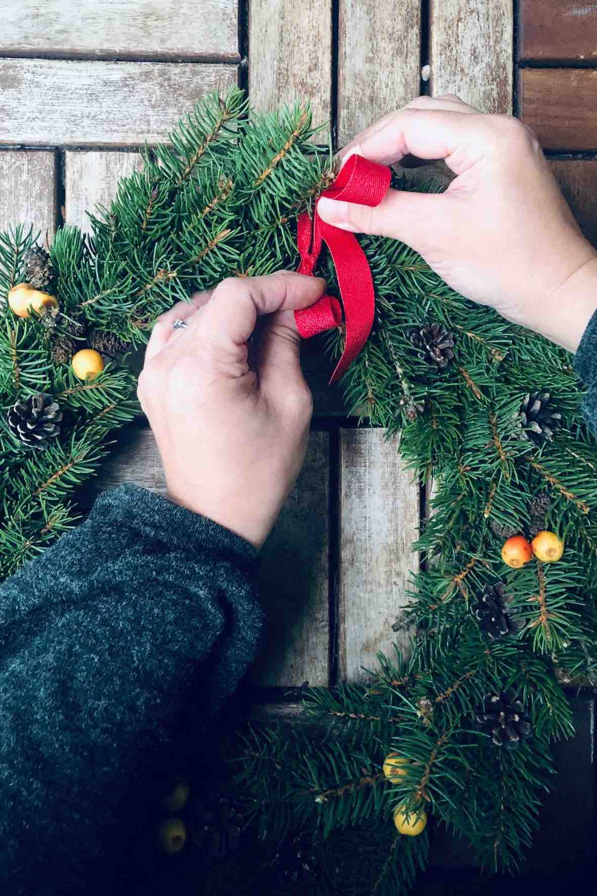 A woman tying a ribbon to a Christmas wreath.