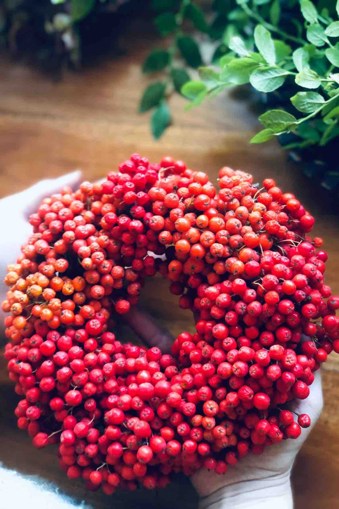 Woman holding a handmade rowan berry wreath in her hands.