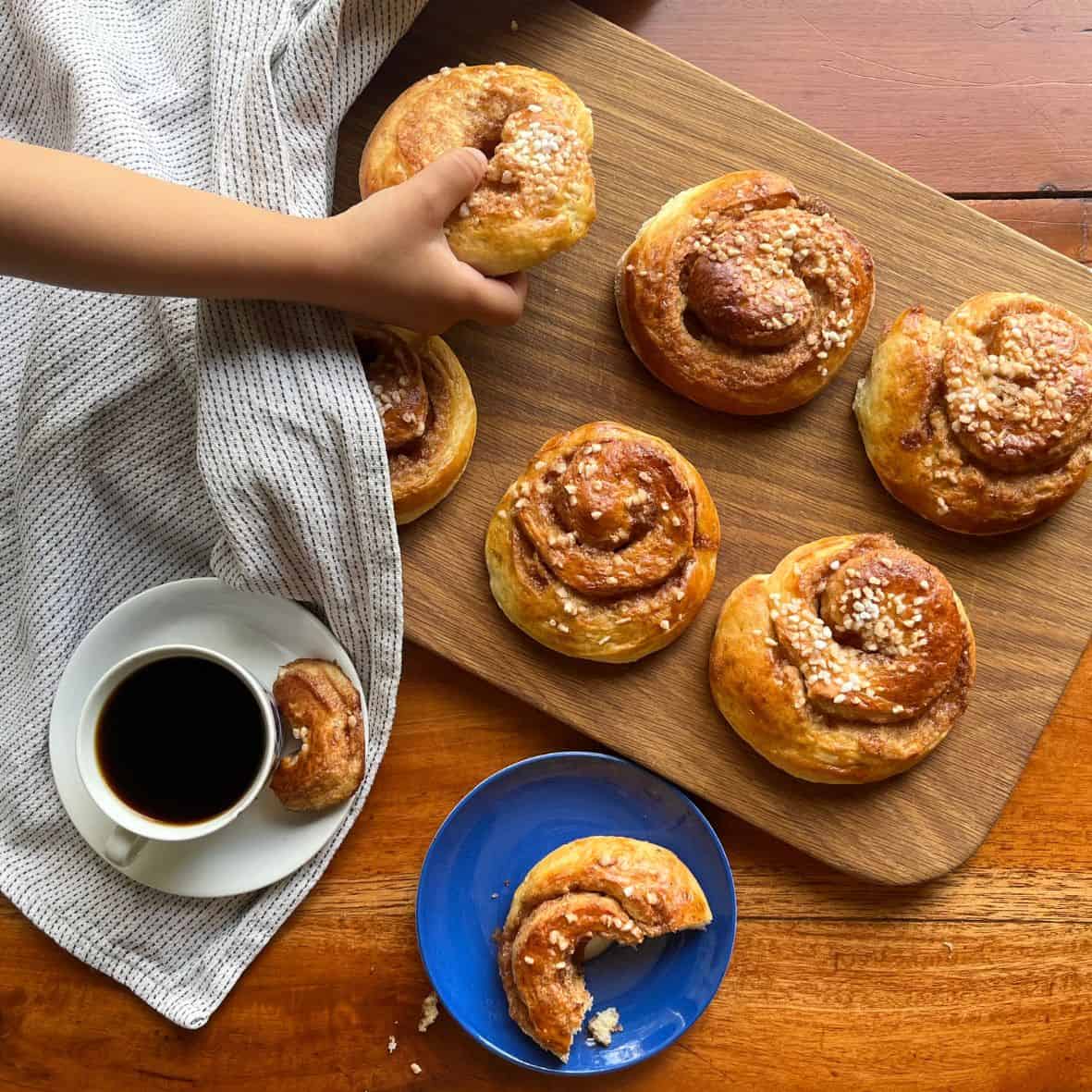 A girl is grabbing one of the yummy-looking Danish cinnamon snails, kanelsnegle, on the serving board on a coffee table. 