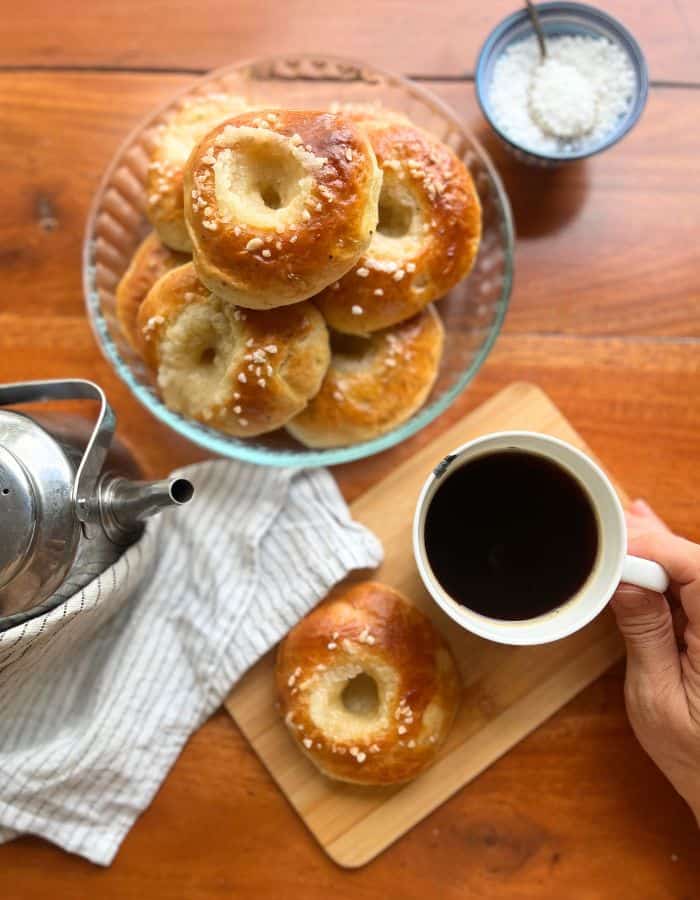 Finnish butter eye buns on a serving plate and a woman holding a coffee cup with one Finnish sweet bun on a wooden plate next to it.