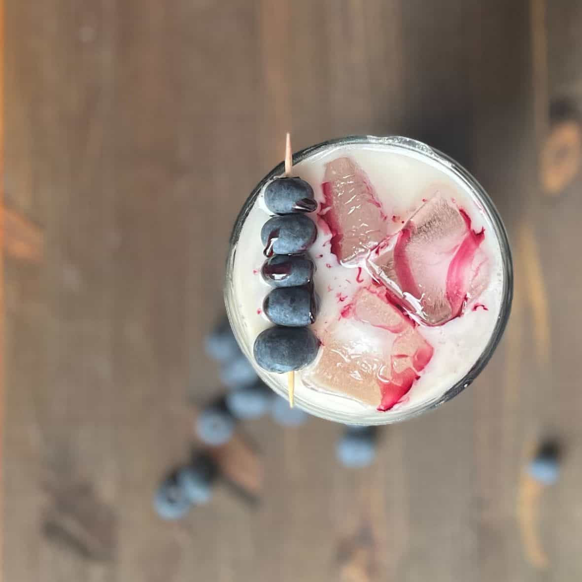 Blueberry iced latte from above with a blueberry cocktail pick garnish and homemade blueberry coffee syrup drizzled oved the ice cubes.