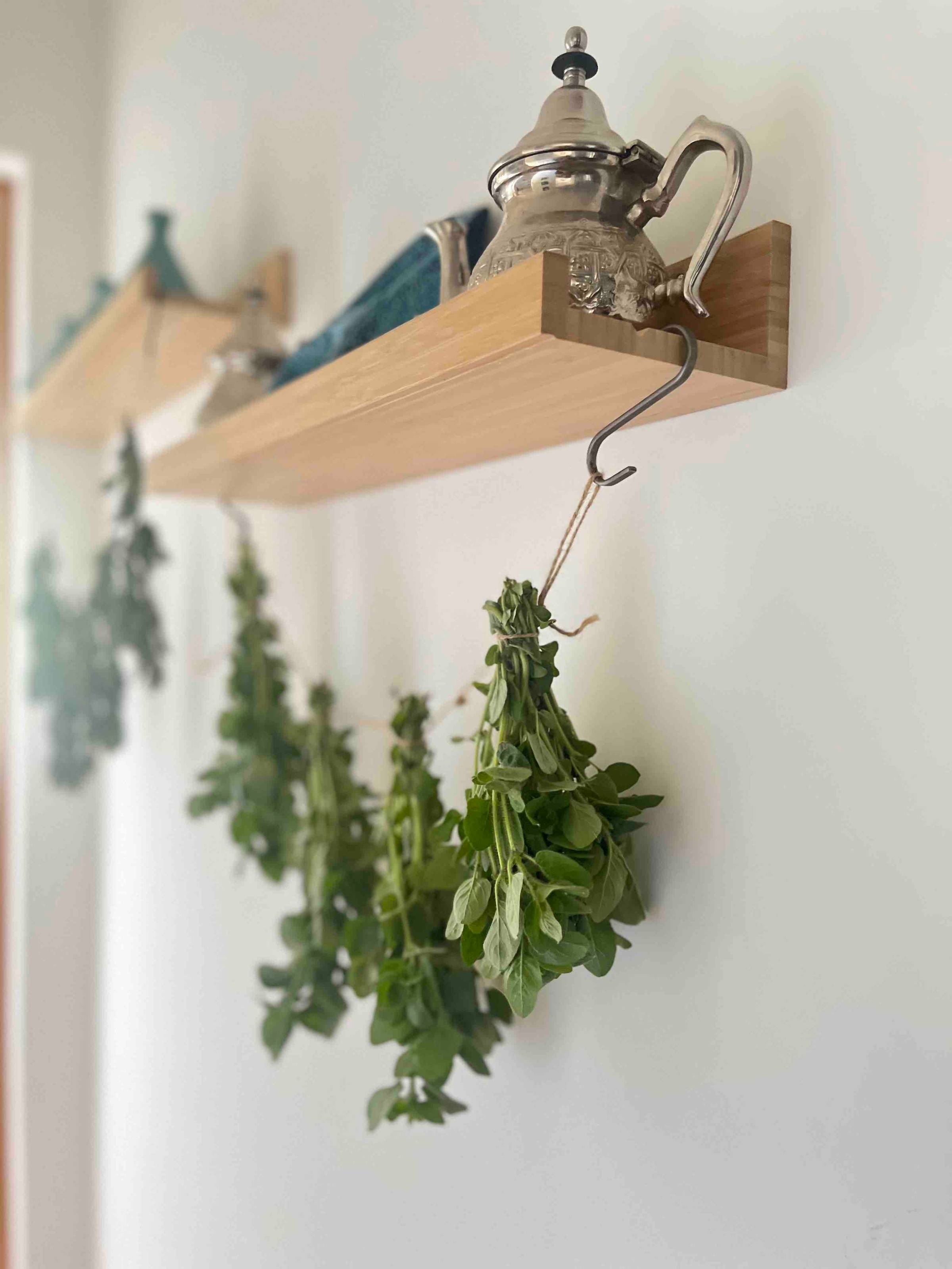 Tiny bouquets of mint drying from the hooks attached to the shelf with a Moroccan teapot on the top.