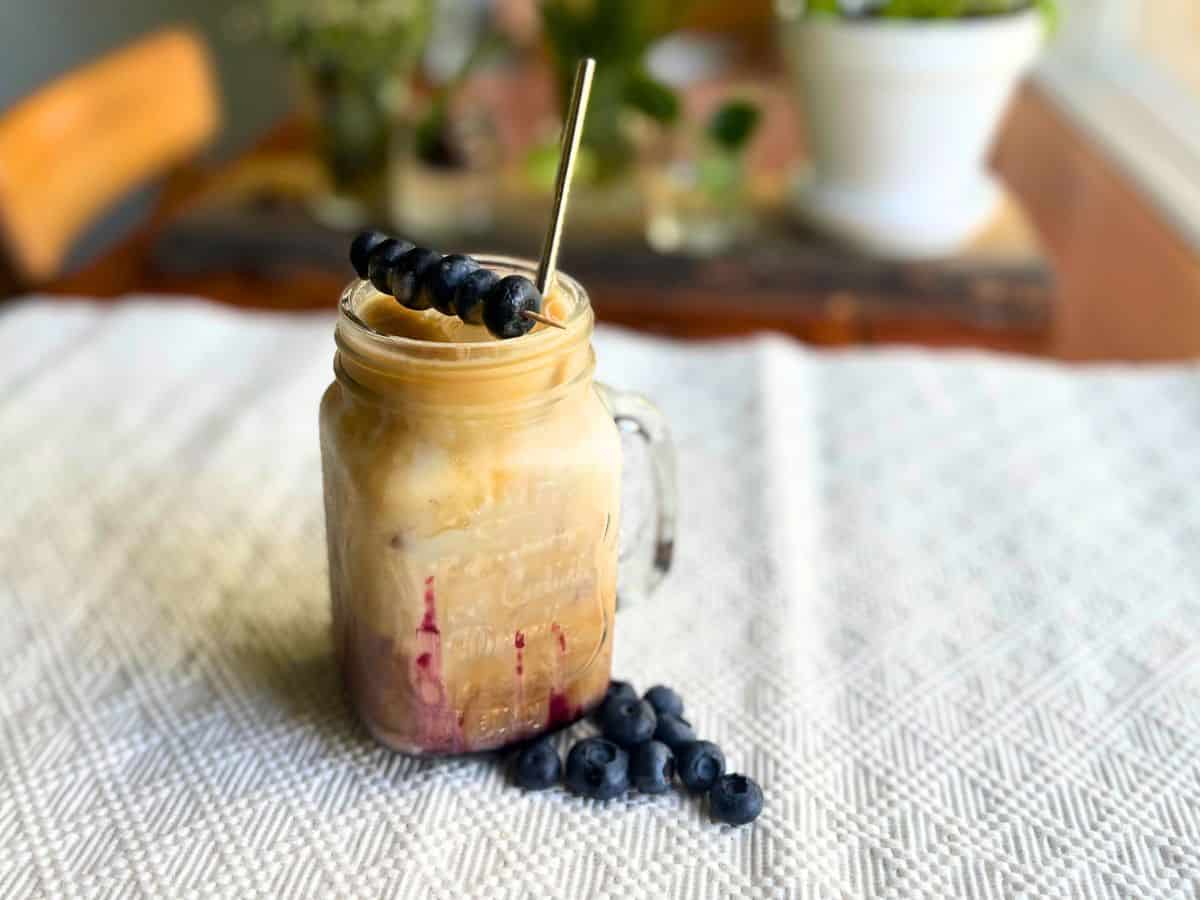Blueberry iced latte in a iced beverage jug with blueberiies as garnish.