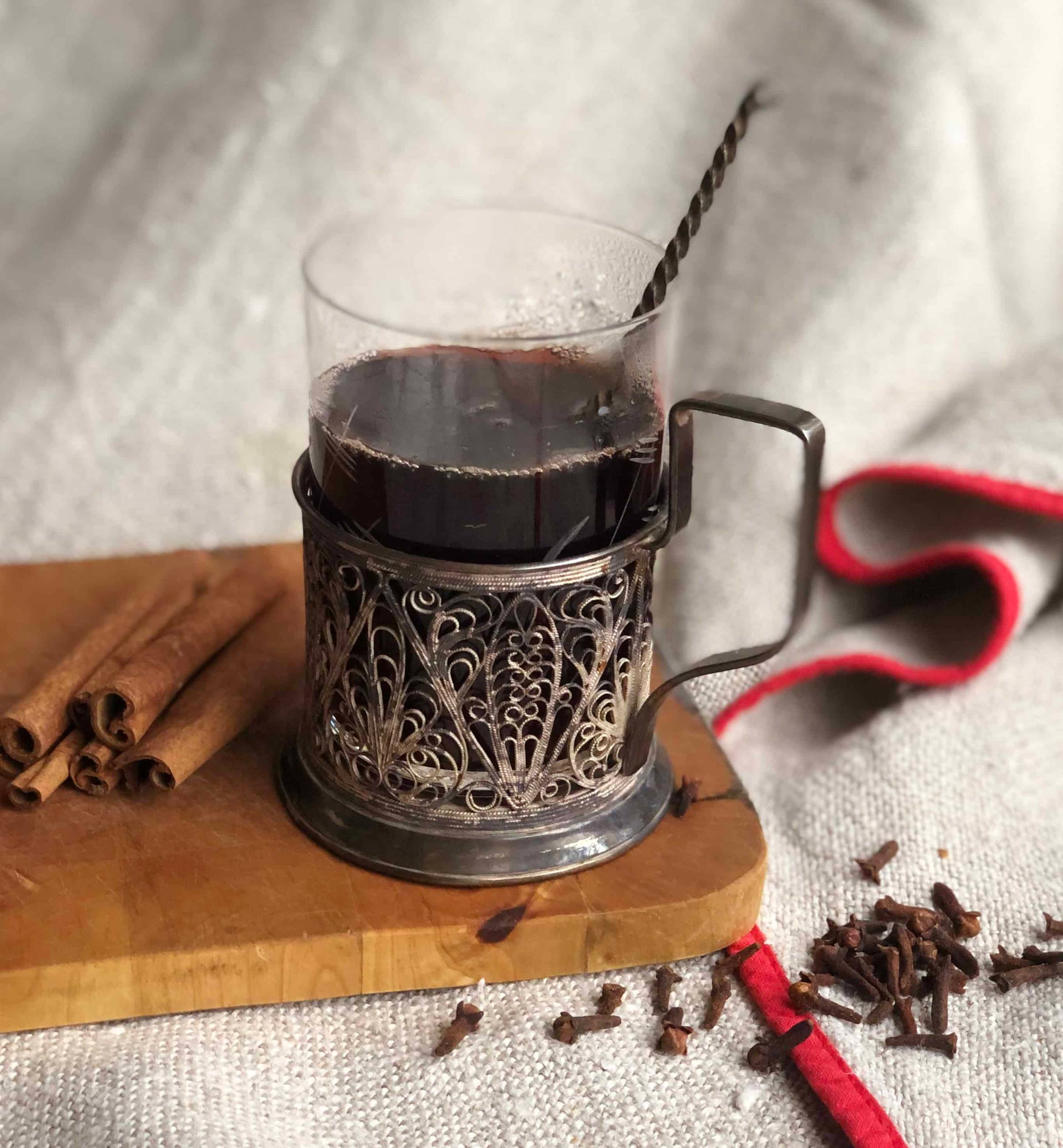 A glass of Nordic Hibiscus glogg on a wooden serving baord with cinnamon sticks.