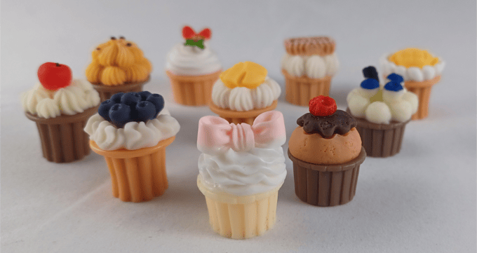 9 different types of resin cupcakes with fruit, chocolate frosting, or bows on different cupcakes