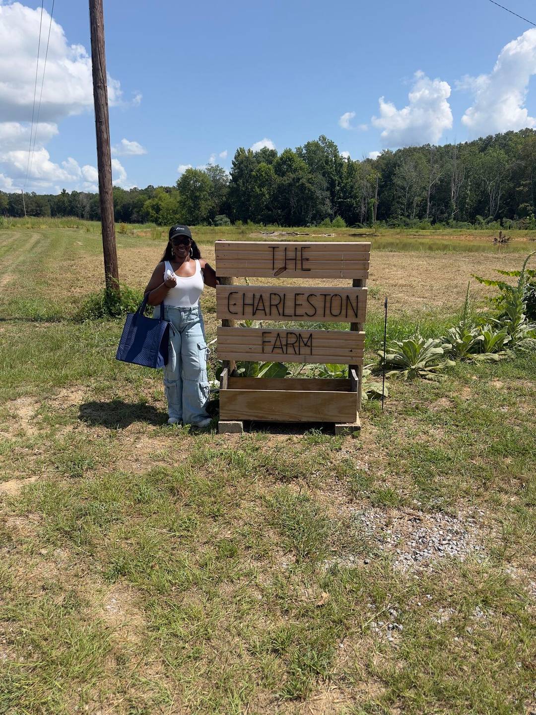 Vannesia standing next to a sign that reads "The Charleston Farm"