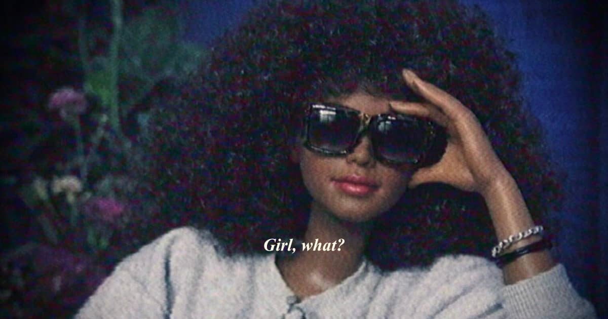 A Barbie with curly hair wears oversized sunglasses and raises one hand to her forehead in a playful, skeptical expression. White text over the image reads, “Girl, what?”