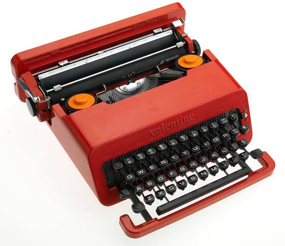 A red Olivetti Valentine portable typewriter shown open from above, revealing its mechanical components and keyboard with white and black keys