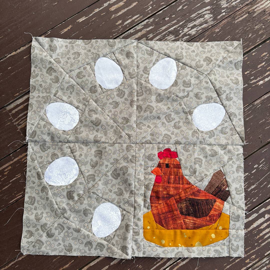 a foundation paper pieced block featuring a chicken and eggs in a wreath style on a brown background