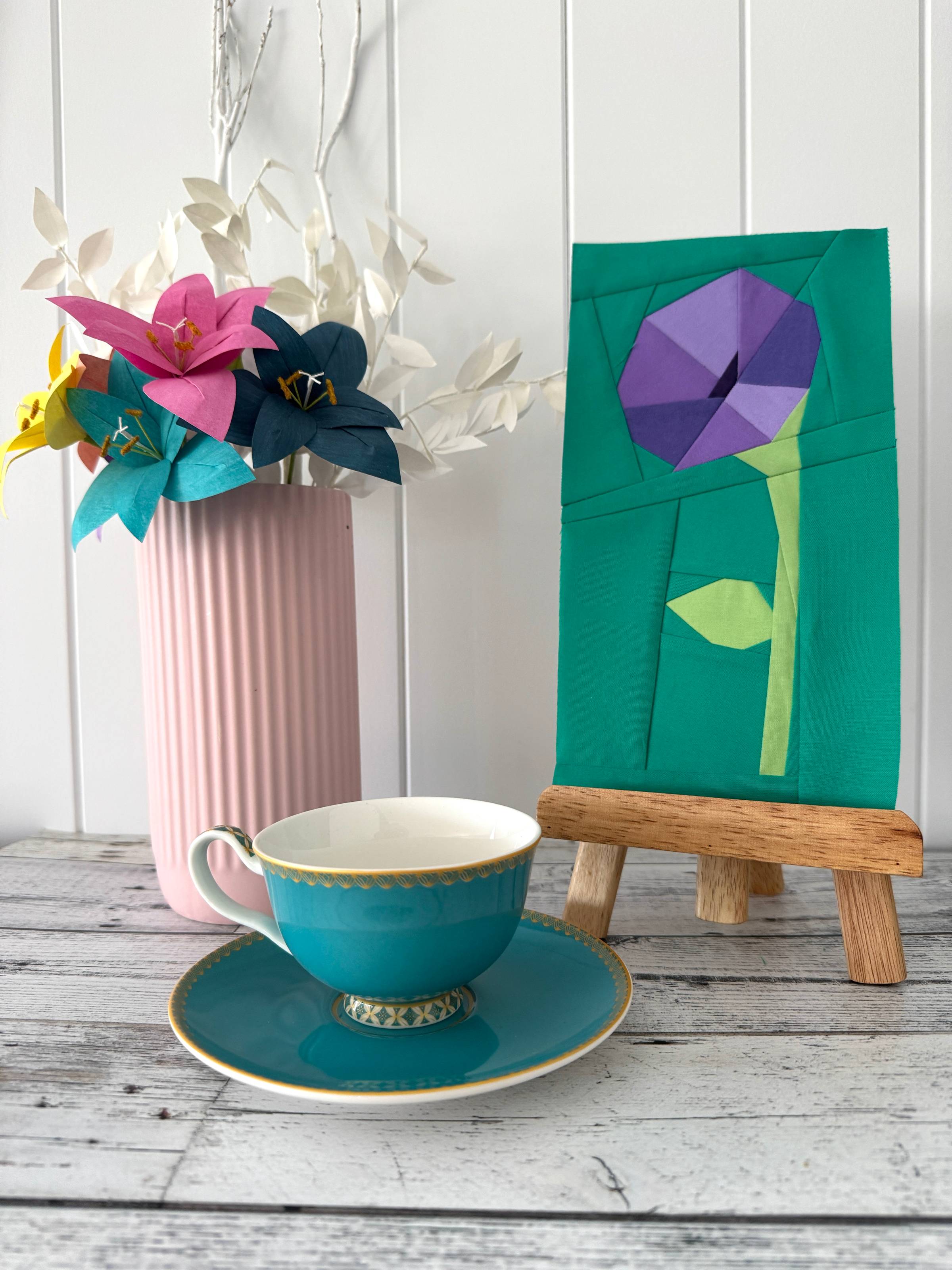a paper pieced block featuring a morning glory flower shown with a vase of paper flowers and a teacup
