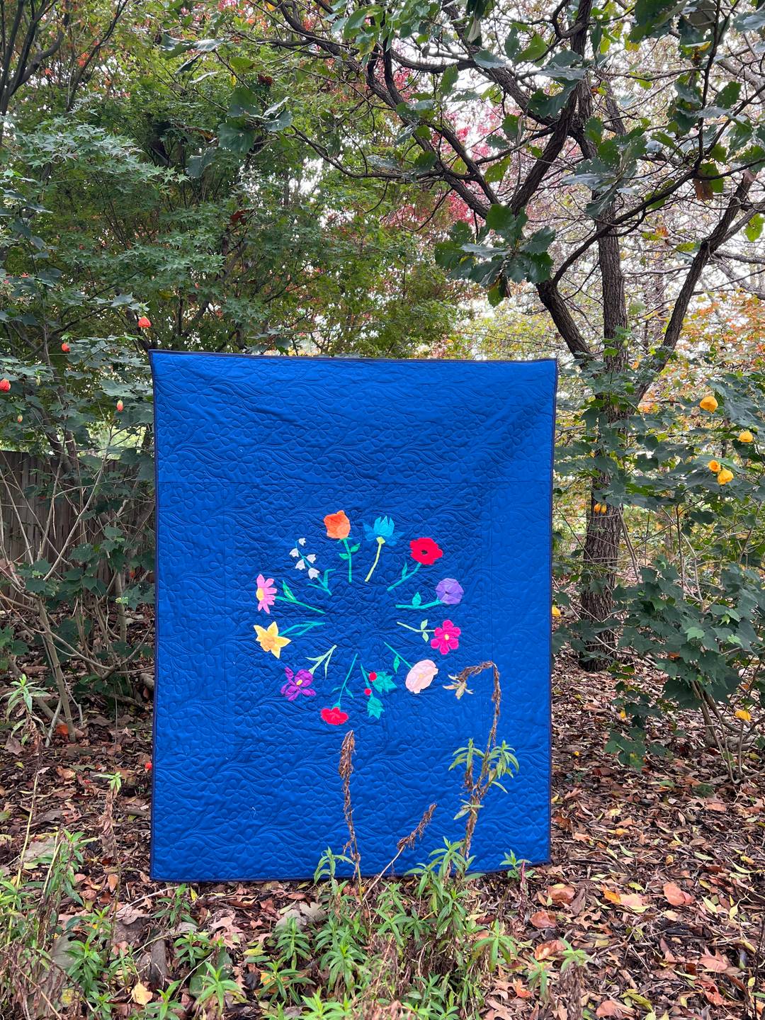 A quilt featuring a wreath of 12 different flowers on a navy background