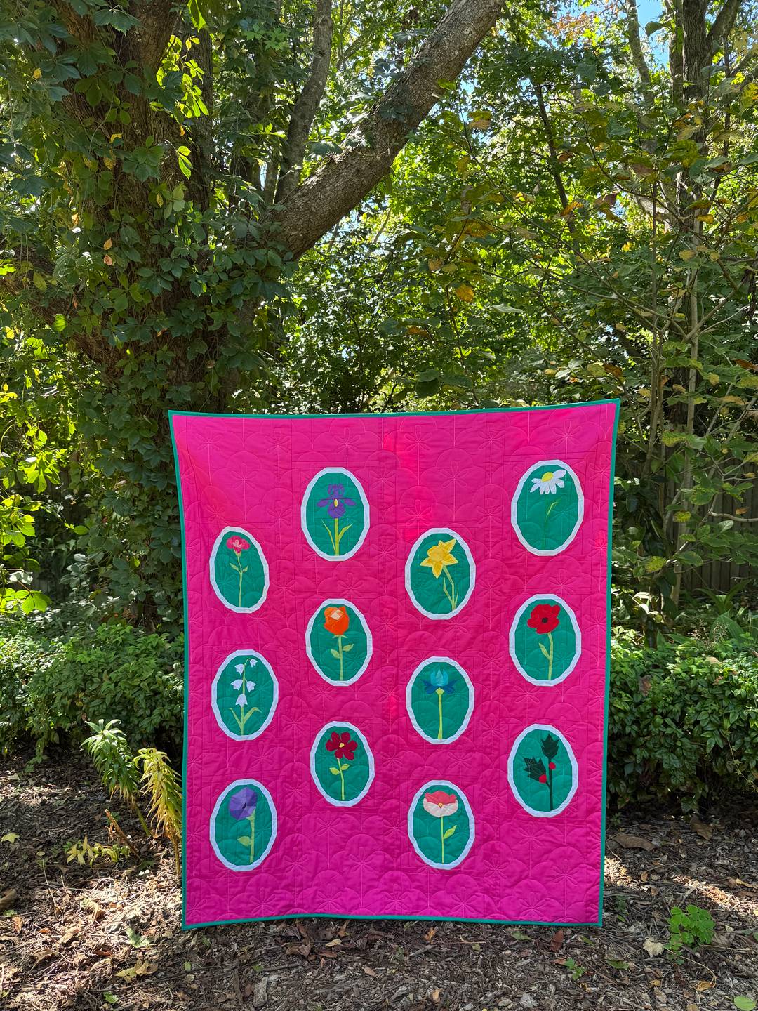 a quilt featuring twelve flowers framed in white on a hot pink background