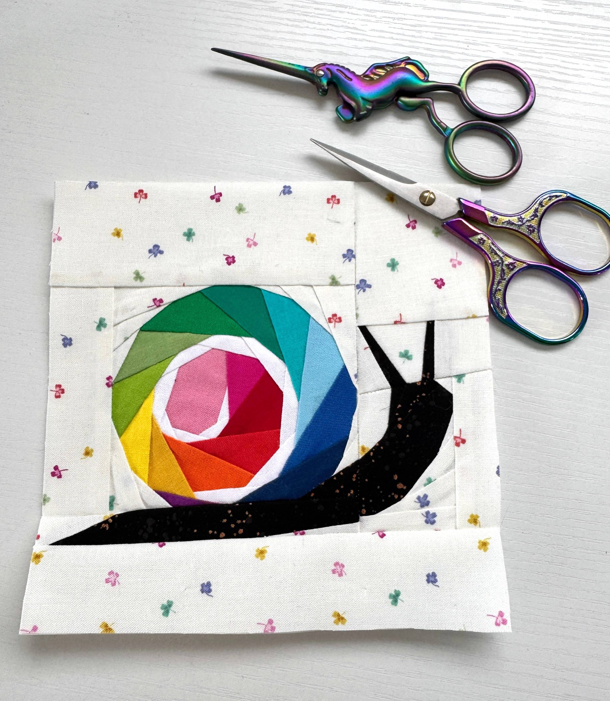 a foundation paper pieced block featuring a snail with a rainbow shell with a white swirl on a background of clover fabric