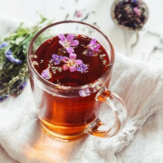 a glass mug filled with tea next to a bunch of flowers