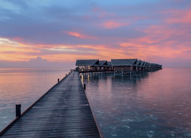 Wooden boardwalk over water to chalets with pink sunset sky