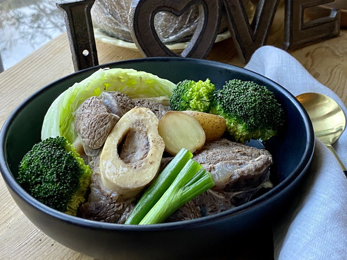 beef shanks with broccli, cabbage and green onion in a black bowl