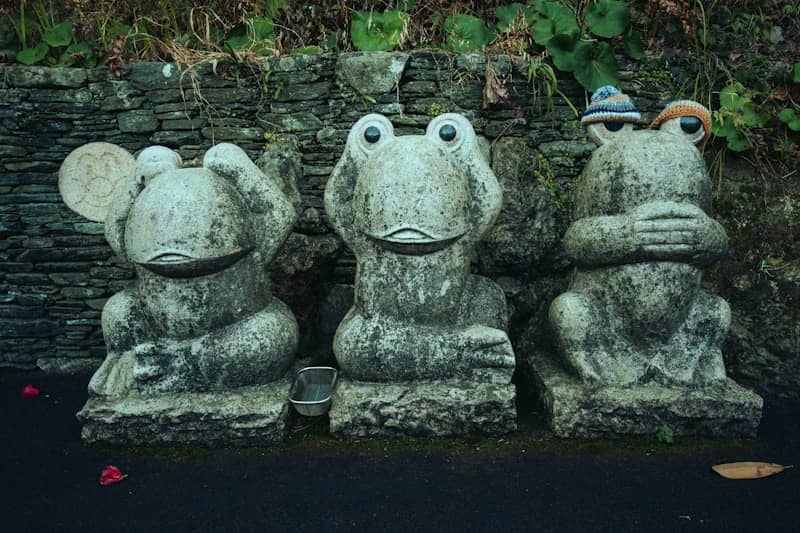 Three stone frog statues covering eyes, ears, and mouth.