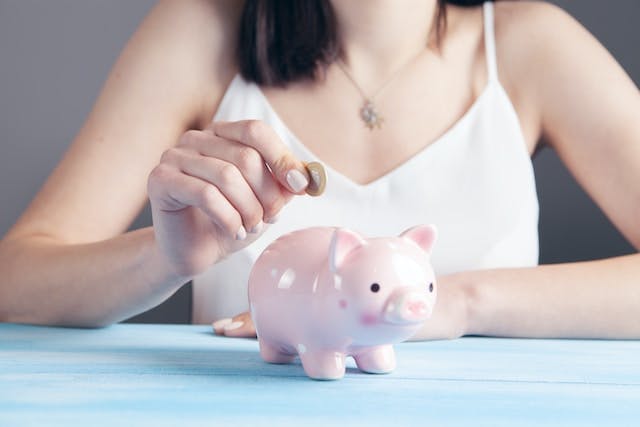 Closeup of woman hand putting a coin into a piggy bank.