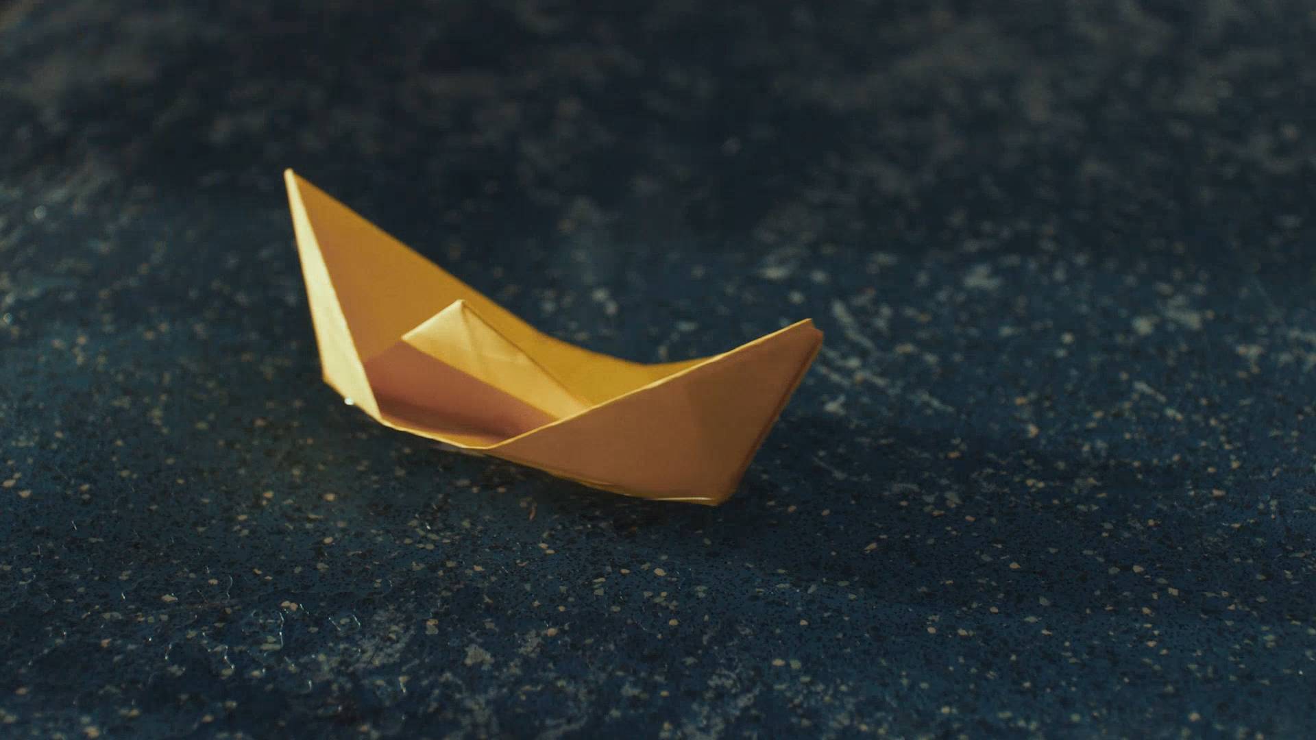 A yellow paper boat floats in a puddle