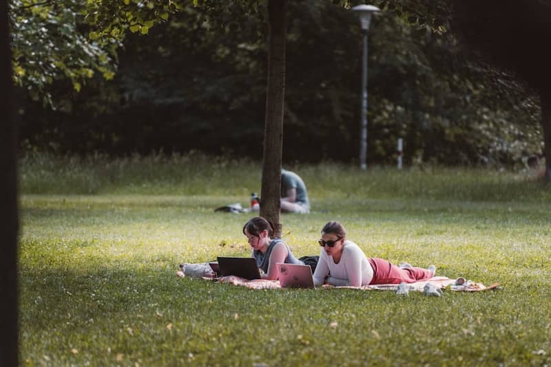 Two women reading on a blanket in a park.