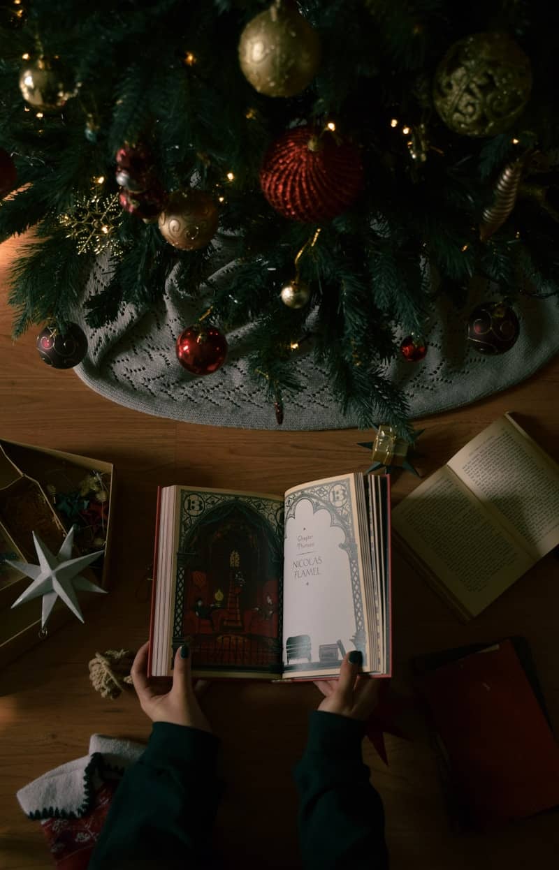 A person reading a book in front of a christmas tree