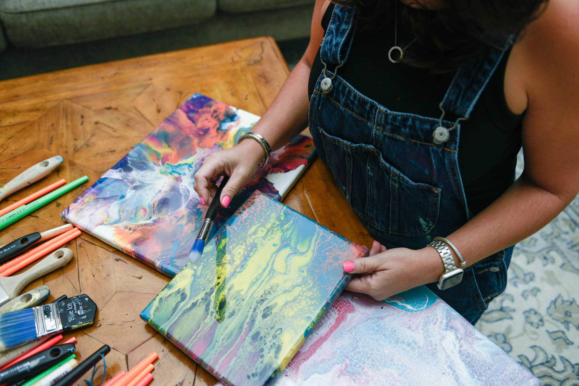 picture of artist looking art different art supplies and paint pour on canvas